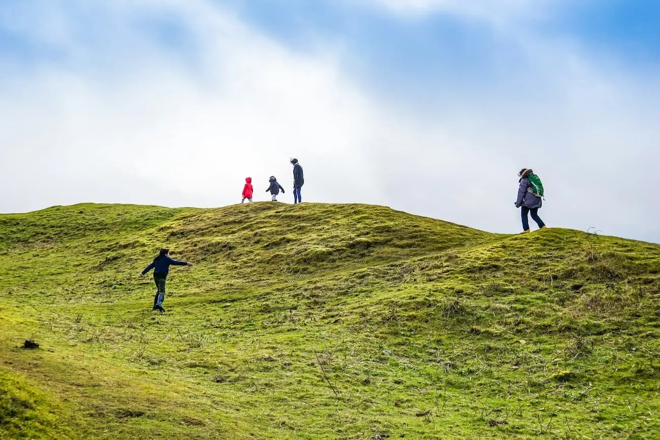 Several people ascending a grassy hill, engaged in conversation and appreciating the natural landscape around them.