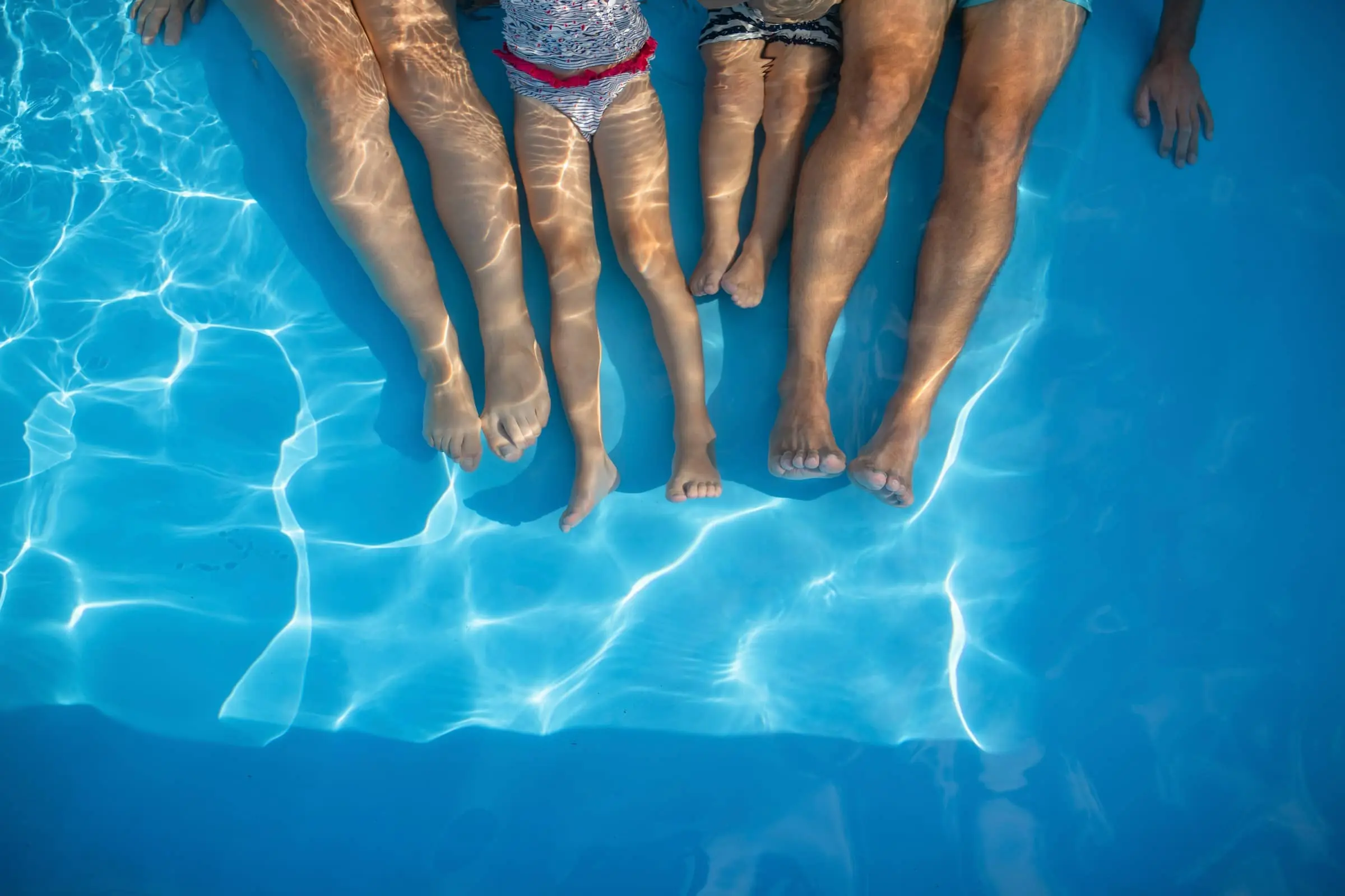 Image of a family sitting by the pool. Only their legs are visible.